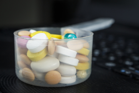 Pile of pills in a plastic measuring spoon on the keyboardの写真素材