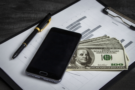 Black ballpoint pen with a bunch of dollars and a mobile phoneの写真素材