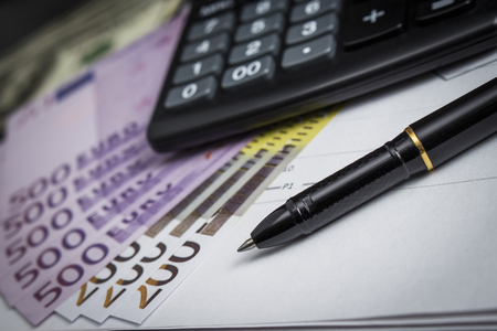 Black ballpoint pen with a bunch of euros and a calculatorの写真素材