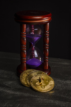 Coins in the form of bitcoin near the hourglassの写真素材