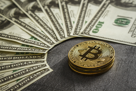 Coins in the form of bitcoin on a dark wooden table near the dollarsの写真素材