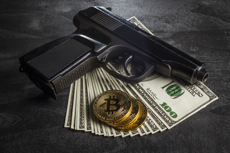Gold coin in the form of bitcoin with dollars and a gunの写真素材