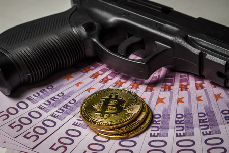 Black pistol with a pack of euros and coins in the form of bitcoin on a white tableの写真素材