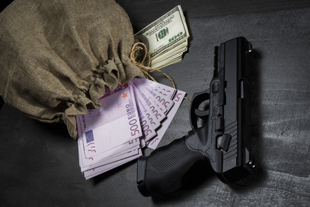 Pistol on the table near the bag with dollars and eurosの写真素材