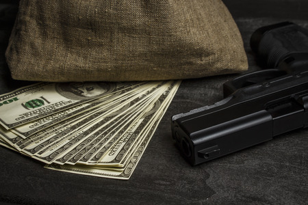 Pistol on the table near the bag with dollarsの写真素材
