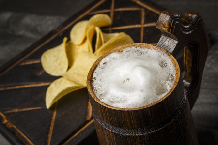 Beer in a wooden mug with chips on the boardの写真素材