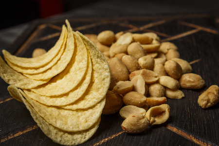 Peanuts and chips on a dark wooden board