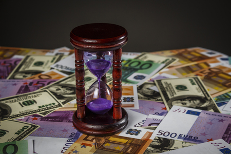 hourglass stand on a pile of dollars and euros