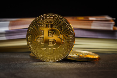 Coins in the form of bitcoins near packs of dollars and eurosの写真素材
