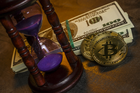 Hourglass with wad of dollars and gold coins in the form of bitcoinの写真素材