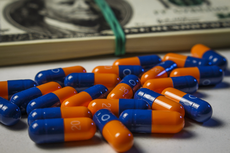 Blue-orange capsules with a pack of dollars on a white doctor's tableの写真素材