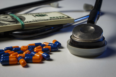 Blue-orange capsules with a pack of dollars and a phonendoscope on a white doctor's table