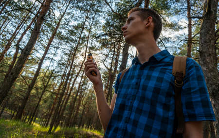 A young man in a blue plaid shirt and a backpack walks through the coniferous forestの写真素材