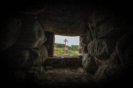 Window in an old stone wall; a wooden cross is visible in the openingの写真素材