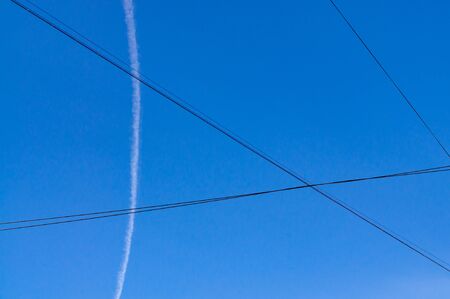 abstract background with crossed wires, blue sky and a trace from the planeの写真素材