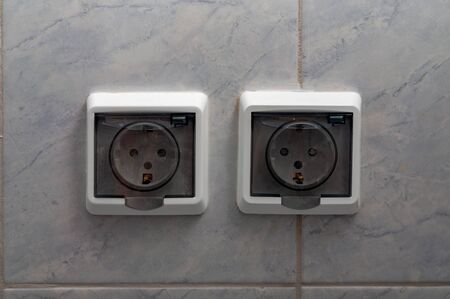 Two sockets with transparent protective plastic cover on tiled wall