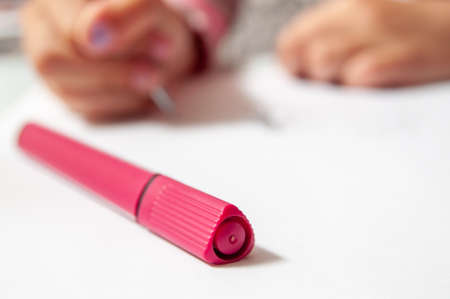 in the foreground is a red marker pen. in the background in the area of blurring hands holding a pen and writing something. photo on the subject of educationの写真素材