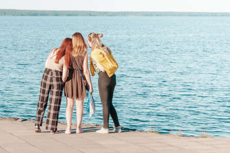 view from the back of three girls standing on the shore of the lake on a summer day.の写真素材