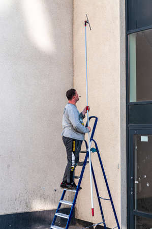 Petrozavodsk, Russia - 3 June 2020. Man on a ladder washes windows using a scraper on a long handleのeditorial素材
