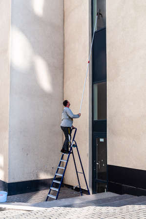 Petrozavodsk, Russia - 3 June 2020. Man on a ladder washes windows using a scraper on a long handle