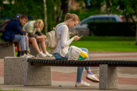 Saint Petersburg, Russia - 22 Augusr 2019. Young girl sits on a bench and looks into the phoneのeditorial素材