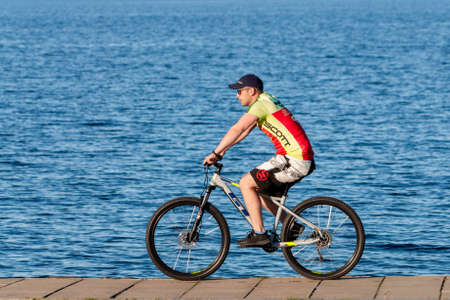 Petrozavodsk, Russia - 13 Juny 2020. Handsome athletic man on a bike rides along the edge of the...
