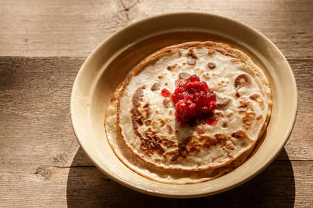 plate with Russian pancakes and cranberry jam on wooden backgroundの写真素材