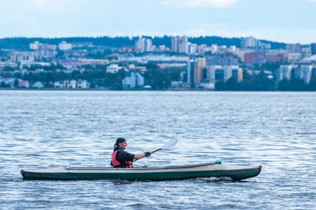 Petrozavodsk, Russia - 2 August 2020. man kayaking on a big lake against the city