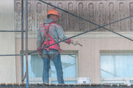 Petrozavodsk, Russia - 17 August 2020. a worker paints the facade of the building. View through the...
