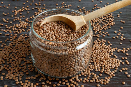 wooden spoon in glass jar full of lentils on dark background