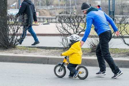 Petrozavodsk, Russia - 1 May 2021. Father helps his child to ride on the balance bicycle