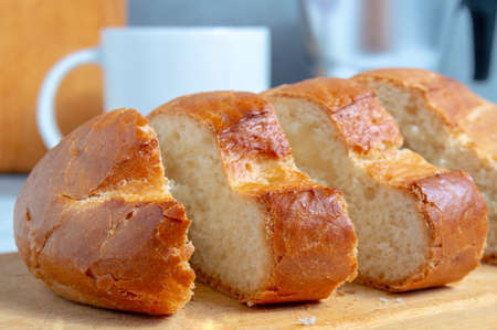Pieces of bun on a cutting board against a coffee maker and a cup