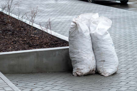 Several large white plastic bags full of garbage on the clean paved sidewalk