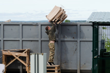 Petrozavodsk, Russia - 26 May 2021. Man throws packing cardboard into large container for construction debrisのeditorial素材