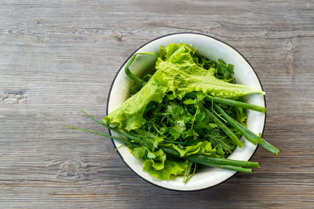 fresh herbs for salad. green onions, parsley, dill and lettuce in a bowl on a gray wooden background. High quality photoの写真素材