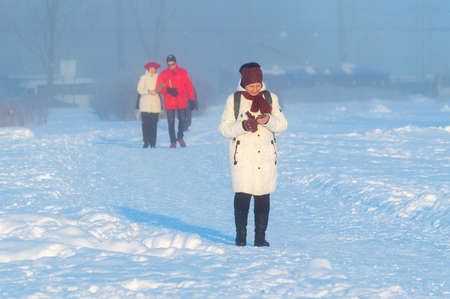 an elderly woman types a message on her phone on a frosty winter dayのeditorial素材