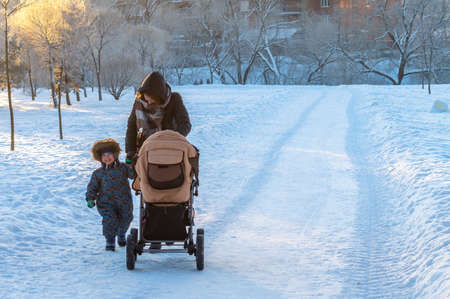 a woman with a child and a stroller in a winter evening parkのeditorial素材