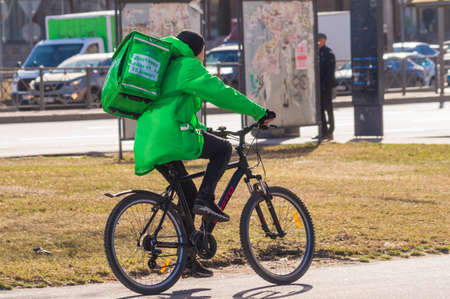 Saint Petersburg, Russia - 21 April 2022. courier in a green jacket on a bicycle