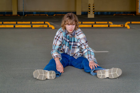 A preteen girl sits on the asphalt in an empty covered parking lotの写真素材