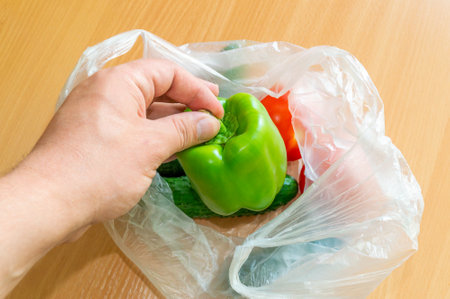Hand puts green pepper in a disposable plastic bag with other vegetablesの写真素材