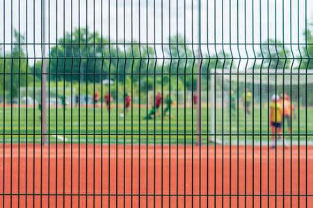 View of a football match through the mesh fence enclosing the stadium. Selective focus. Focus on foregroundの写真素材