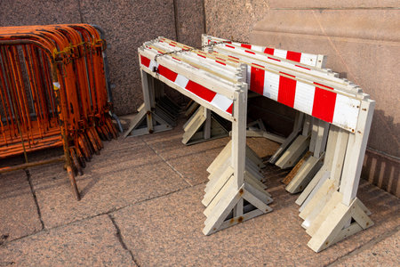 A row of orange and white barricades are stacked on the ground. The barricades are in front of a wall