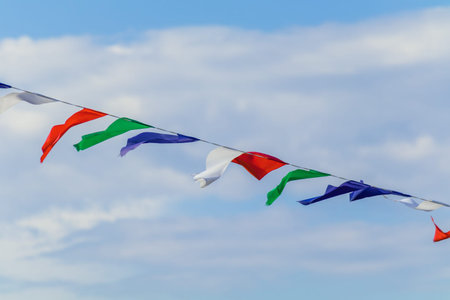 String of bright triangular pennant flags waves in the wind beneath partly cloudy blue sky, creating a light festive outdoor atmosphere with simple color rhythm and open airy composition.