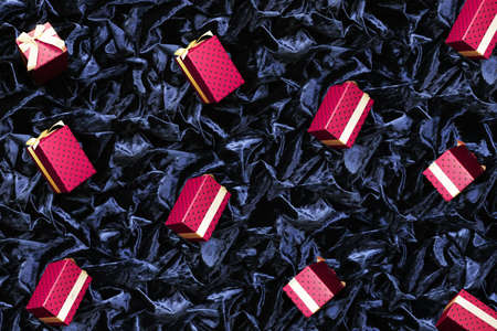 red polka dot gift beautiful festive cardboard boxes with a golden bow on a background of black wrinkled corduroy fabricの写真素材