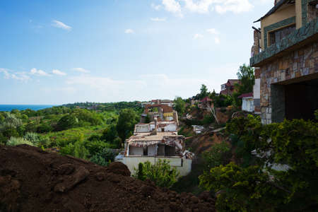 A landslide caused by hurricane rains destroyed expensive cottages and houses. A destroyed house, a summer residence, large cracks, chips, slabs slid down into the abyss. The broken asphalt was displaced by a landslide after the earthquake.の写真素材