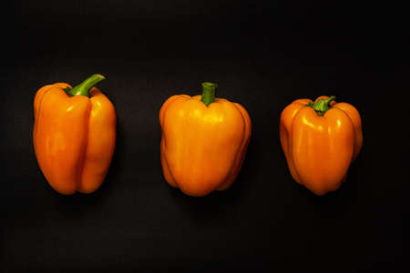 Three moist orange sweet peppers on a black matte work surfaceの写真素材