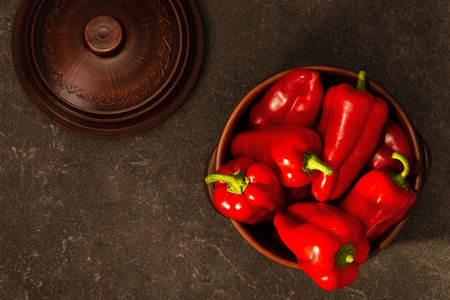 Ripe whole red peppers in a clay bowl. Fresh harvest, traditional cooking ingredient. granite countertop with top viewの写真素材