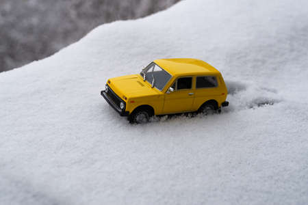 A yellow car got stuck in deep snow. A toy model of an off-road vehicle Vaz 2121 Niva got stuck in a...