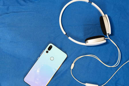 Top view office desk accessories. White headphones and smartphone on blue fabric with copy space.の写真素材