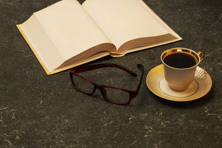 A book, glasses and a cup of coffee on a gray granite table. The habit of reading and drinking...